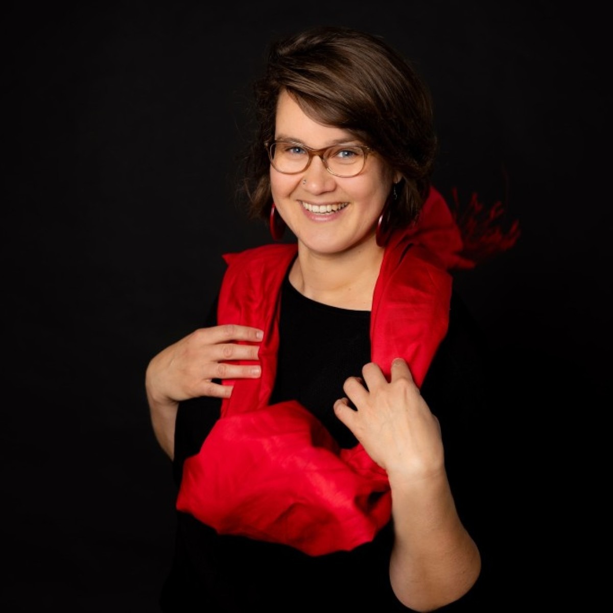 Dorothea blickt lächelnd in die Kamera. Sie hat kinnlange braune Haare und trägt eine beige Brille, rote Ohrringe, einen schwarzen Pulli und ein rotes Tuch.<br />
© Fotomanufaktur Schnittfincke