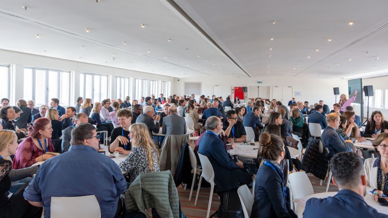 Viele Menschen sitzen an Tischen in einem weiß gehaltenen Raum